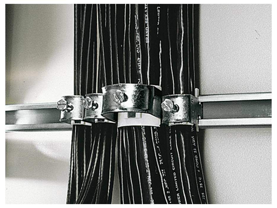 Des agrafes métalliques fixent plusieurs câbles noirs sur un mur blanc. Les câbles sont parallèles et soigneusement rangés.