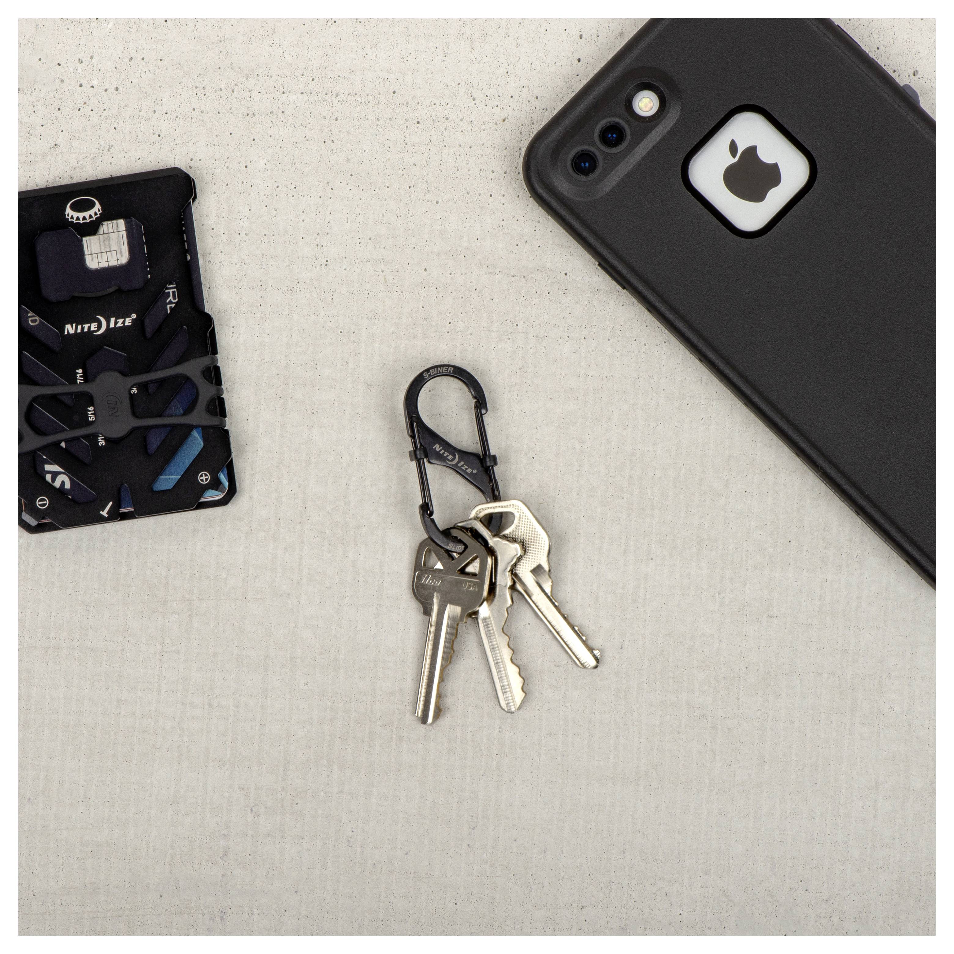 Des clés sur un mousqueton noir, un smartphone avec un logo Apple et un multi-outil sur une surface gris clair.