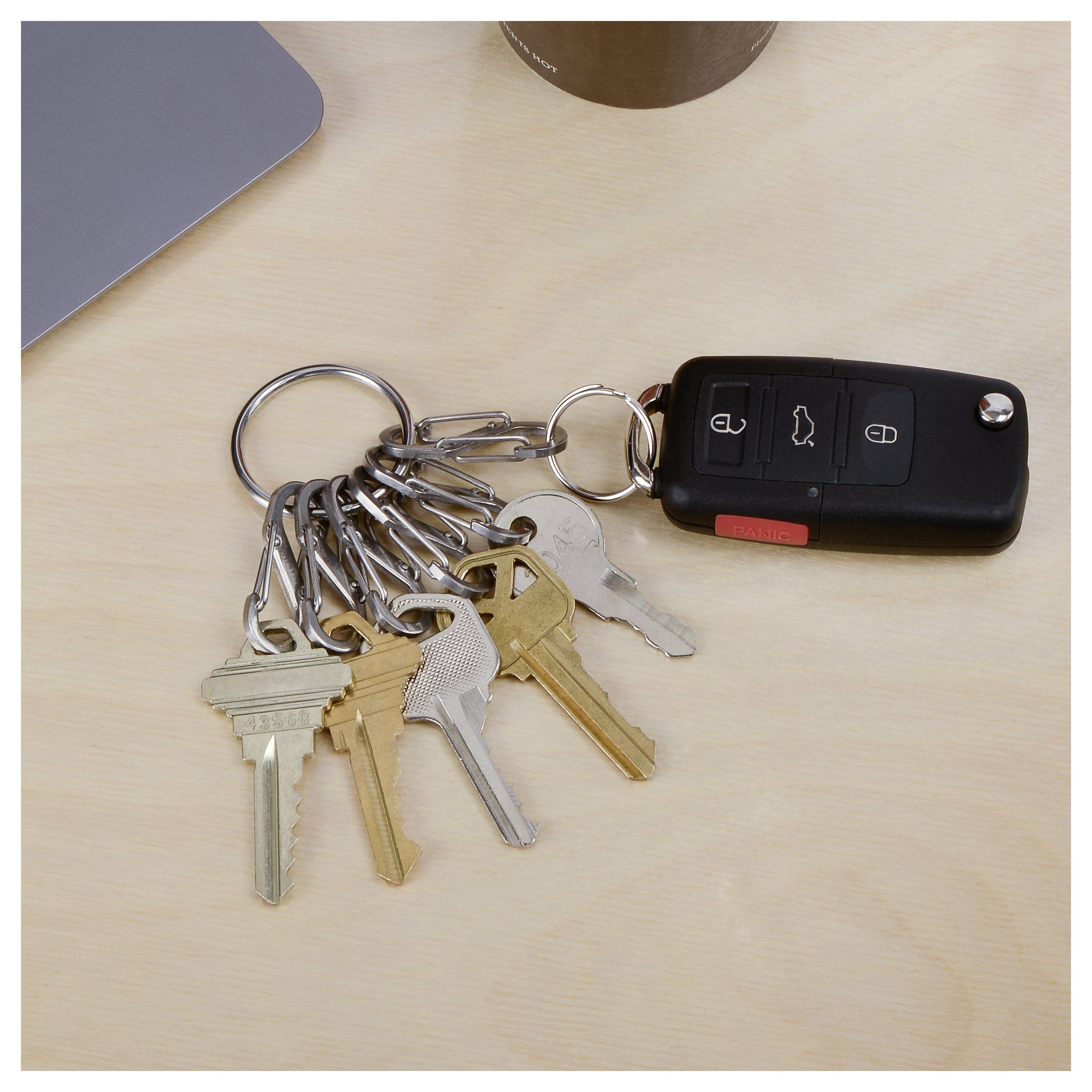 Un ensemble de huit clés sur un anneau de clés avec un porte-clés noir de voiture repose sur une surface en bois clair, près du coin d'un ordinateur portable.