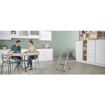 Un couple est assis à la table de la cuisine et feuillette des magazines dans une cuisine moderne aux armoires blanches et au sol gris.