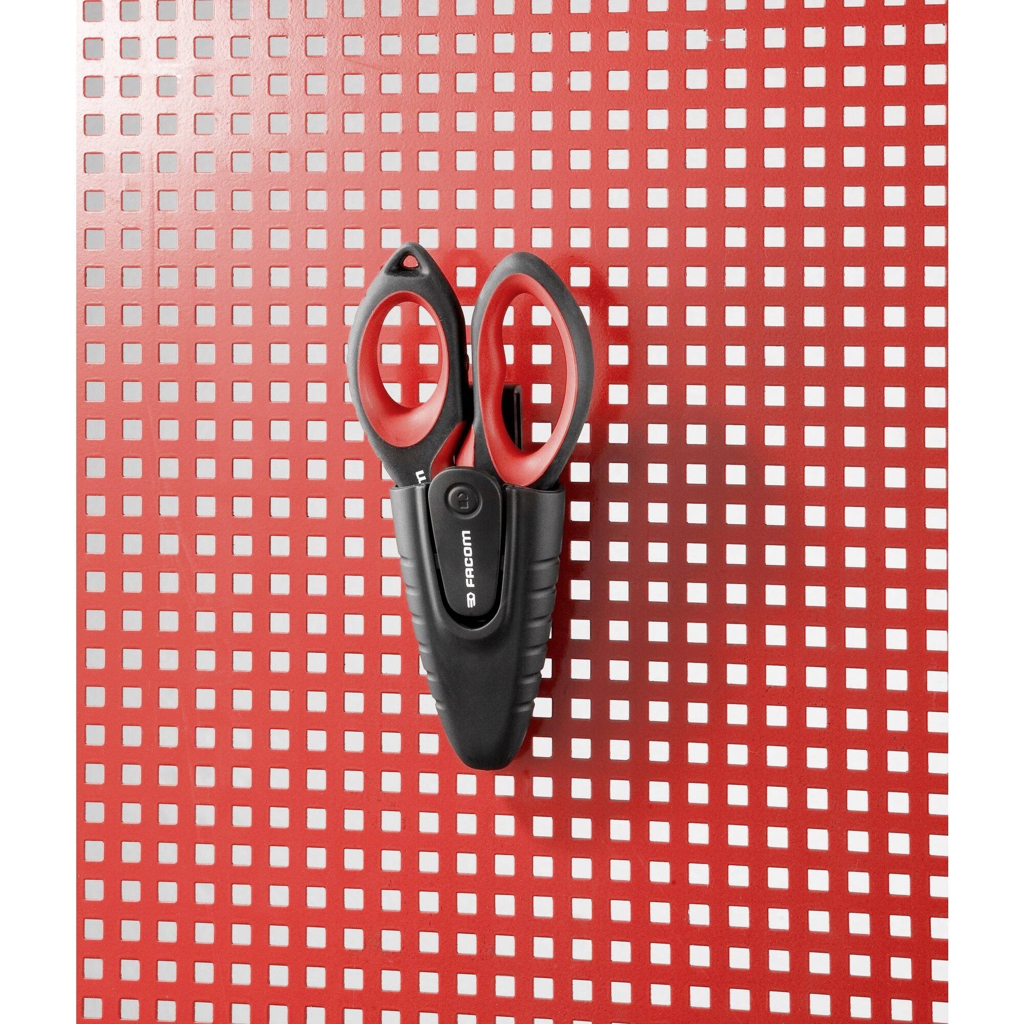 Une paire de ciseaux noirs et rouges est suspendue à un mur perforé rouge avec un motif carré.