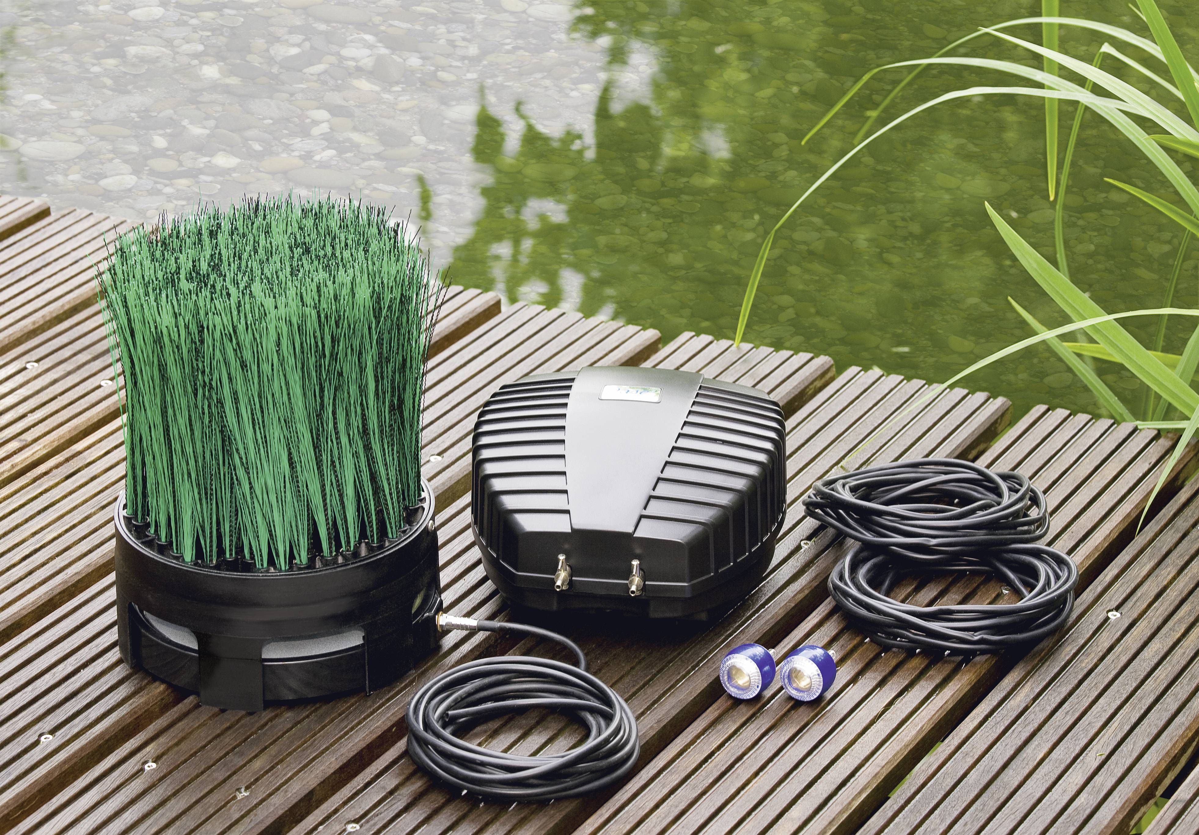 « Kit d'aération pour jardin aquatique sur terrasse en bois, comprenant un diffuseur ressemblant à de l'herbe, une pompe et des tuyaux à côté d'un bassin. »