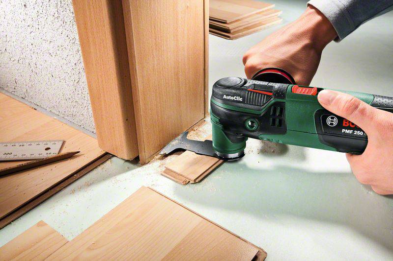 Une personne coupe du bois avec un outil multifonction oscillant sur un chambranle. Des copeaux de bois sont visibles.