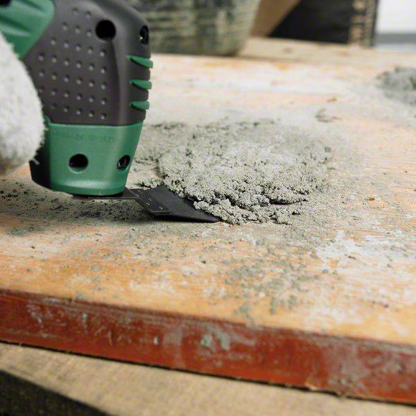 Un gros plan montre une main gantée utilisant une spatule pour enlever l'excédent de béton d'une surface en bois.