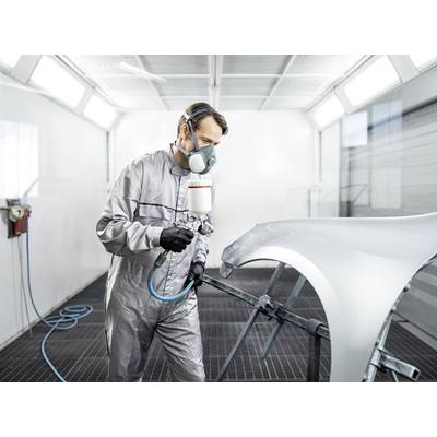 Un homme en combinaison de protection et masque respiratoire peint une pièce automobile dans une cabine de peinture professionnelle.