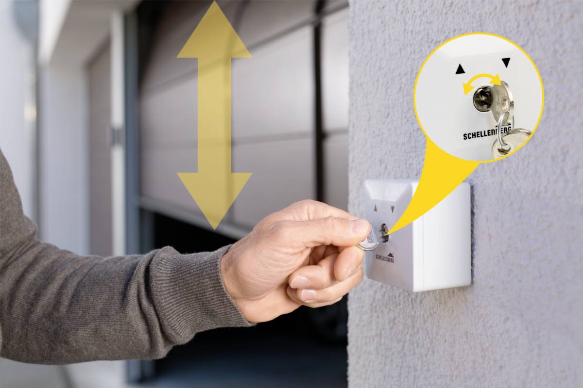 Une main tourne une clé dans l'interrupteur mural pour ouvrir ou fermer un portail de garage. Une flèche jaune indique le mouvement.