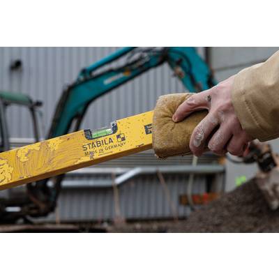 Une personne tient un niveau à bulle sur un chantier de construction. Un excavateur flou est visible en arrière-plan.