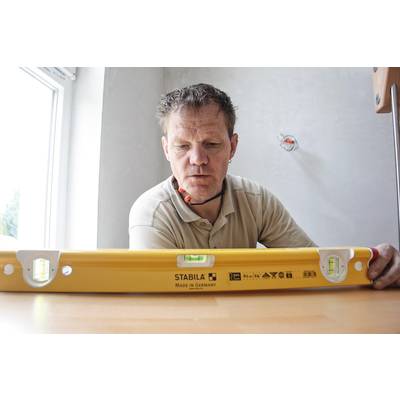 Un homme utilise un niveau à bulle jaune à l'intérieur pour vérifier une surface horizontale.