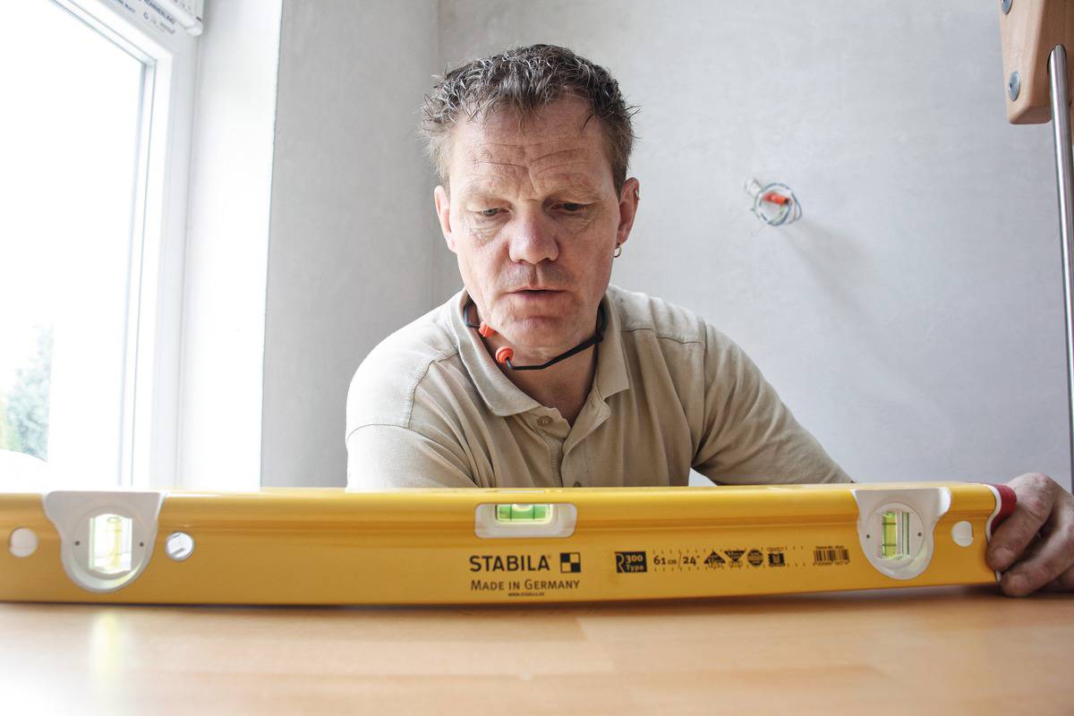 Un homme utilise un niveau à bulle jaune pour mettre un table à niveau. À l'arrière-plan, une fenêtre laisse filtrer la lumière.