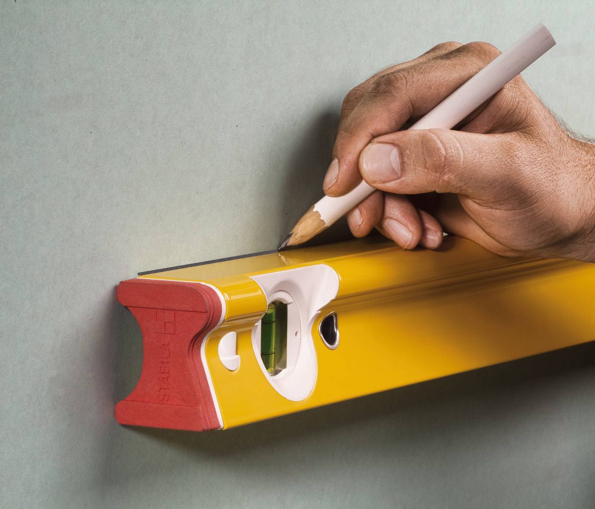 Une main tient un crayon et trace une ligne le long d'un niveau jaune maintenu contre un mur vert.