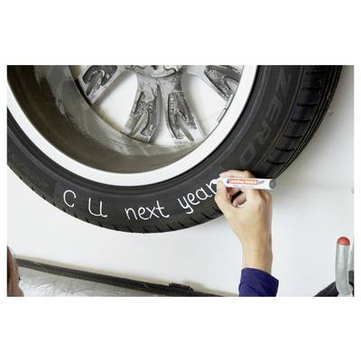 Une main écrit « À bientôt l'année prochaine » sur un pneu de voiture avec un marqueur blanc.