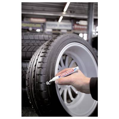 Une main utilise un marqueur blanc pour écrire sur un pneu de voiture dans un magasin de pneus, probablement pour le marquer ou l'étiqueter.