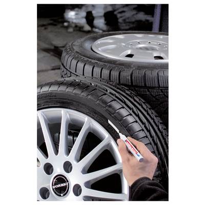 Marquage à la main d'un pneu et d'une roue de voiture avec un marqueur à peinture blanche dans un atelier de pneus.