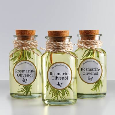 Trois bouteilles en verre d'huile d'olive au romarin, étiquetées 'Huile d'olive au romarin' et munies d'un bouchon en liège, décorées avec une cordelette et des brins de romarin.