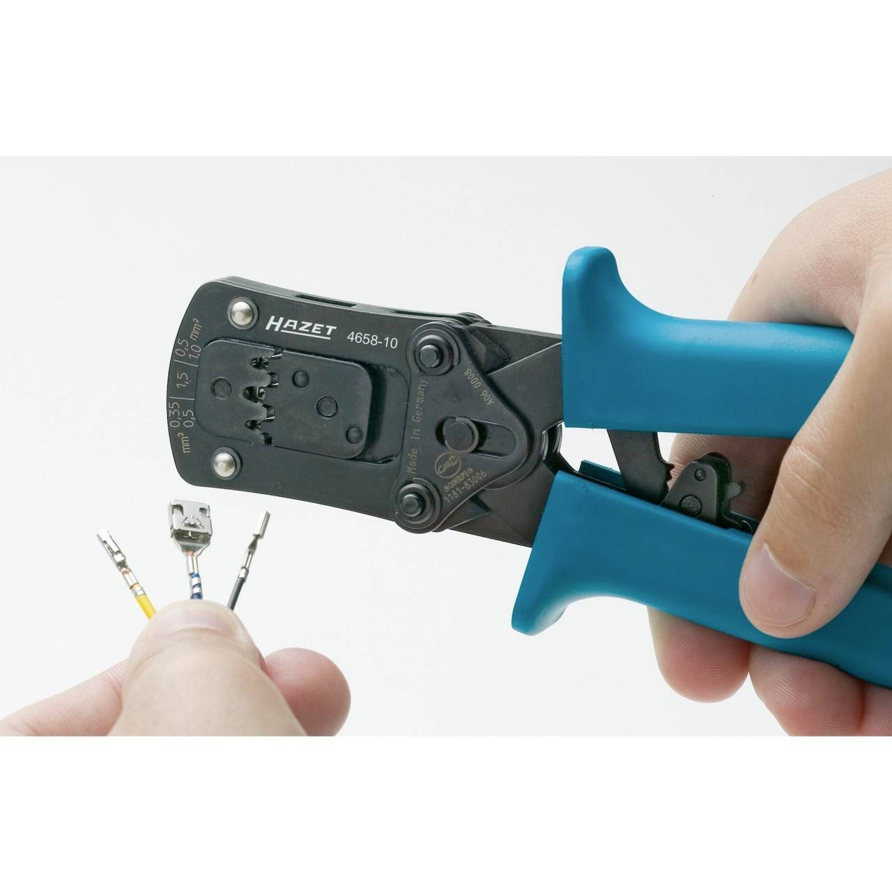 Une main tient une pince à sertir bleue de la marque Hazet, qui est sur le point de fixer des cosses de câble sur un câble.