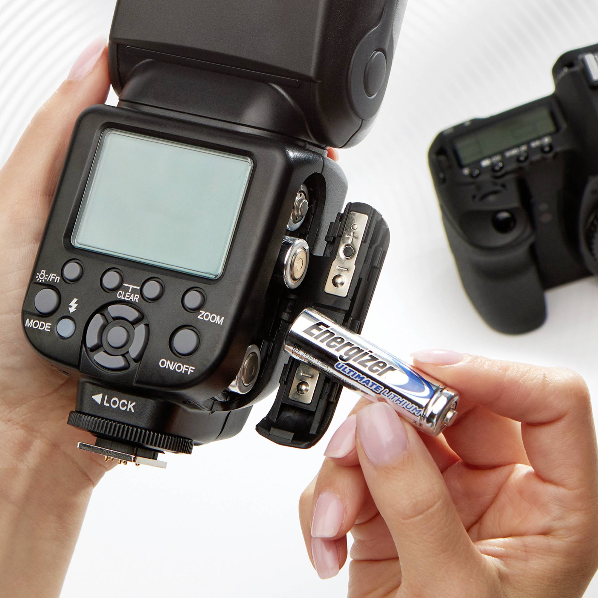 Une personne insère une pile AA dans le compartiment d'un appareil flash qui a été tourné pour ouvrir le compartiment. Un appareil photo est visible en arrière-plan.