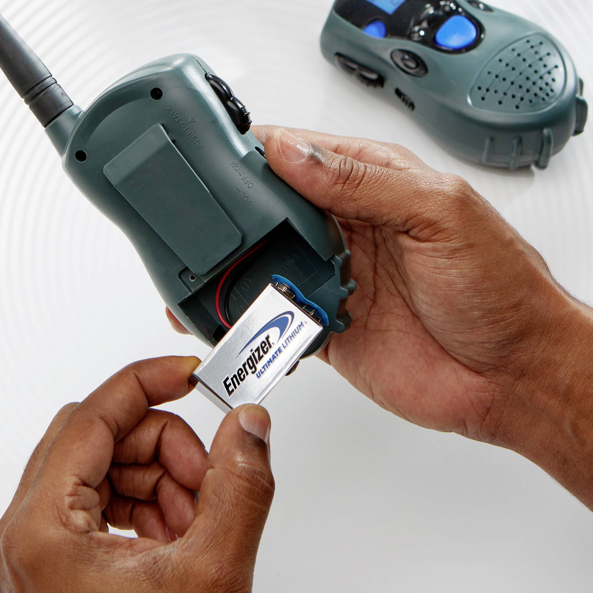 Une personne tient un talkie-walkie et y insère une pile Energizer. Un autre talkie-walkie est posé en arrière-plan.