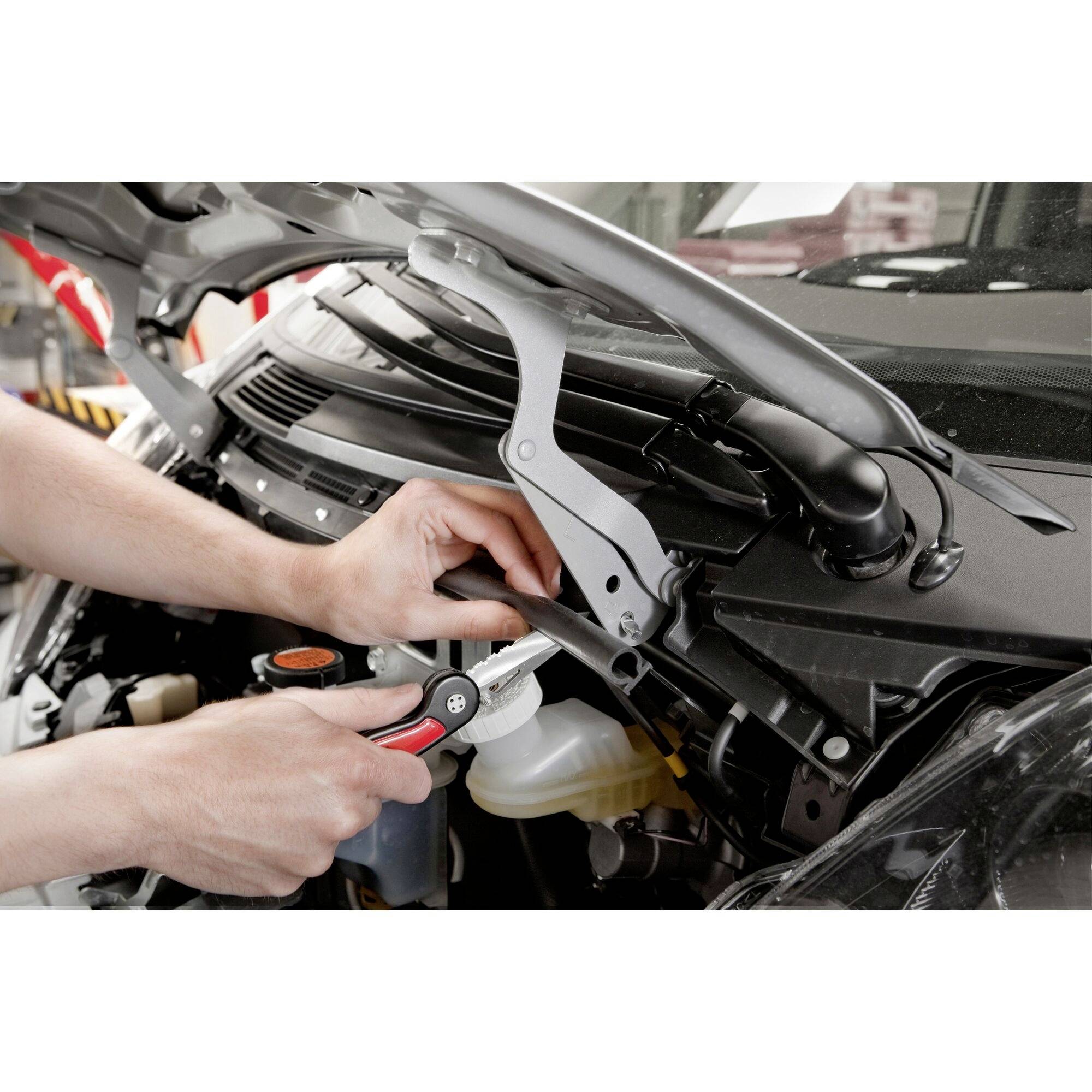 Une personne répare le compartiment moteur d'une voiture avec une clé à molette, alors que le capot est ouvert.