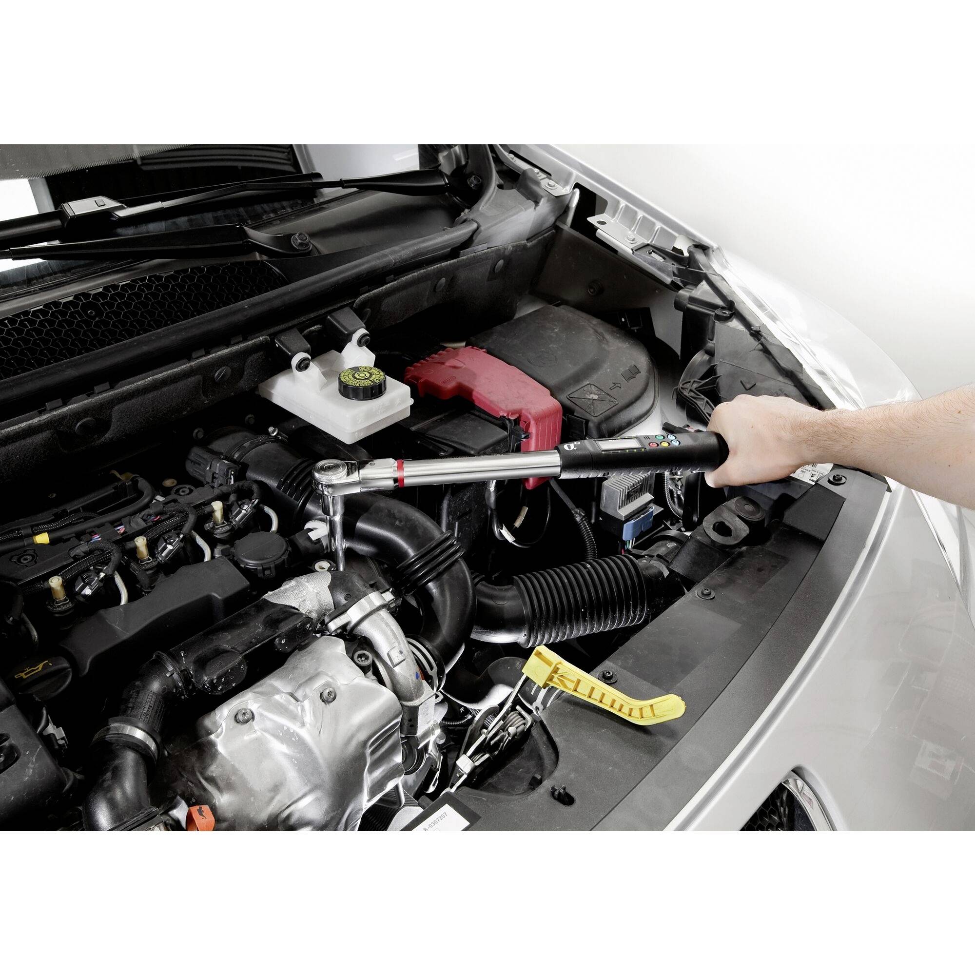 Une personne serre une vis avec une clé dynamométrique dans le compartiment moteur d'une voiture. Le compartiment moteur est ouvert et bien éclairé.