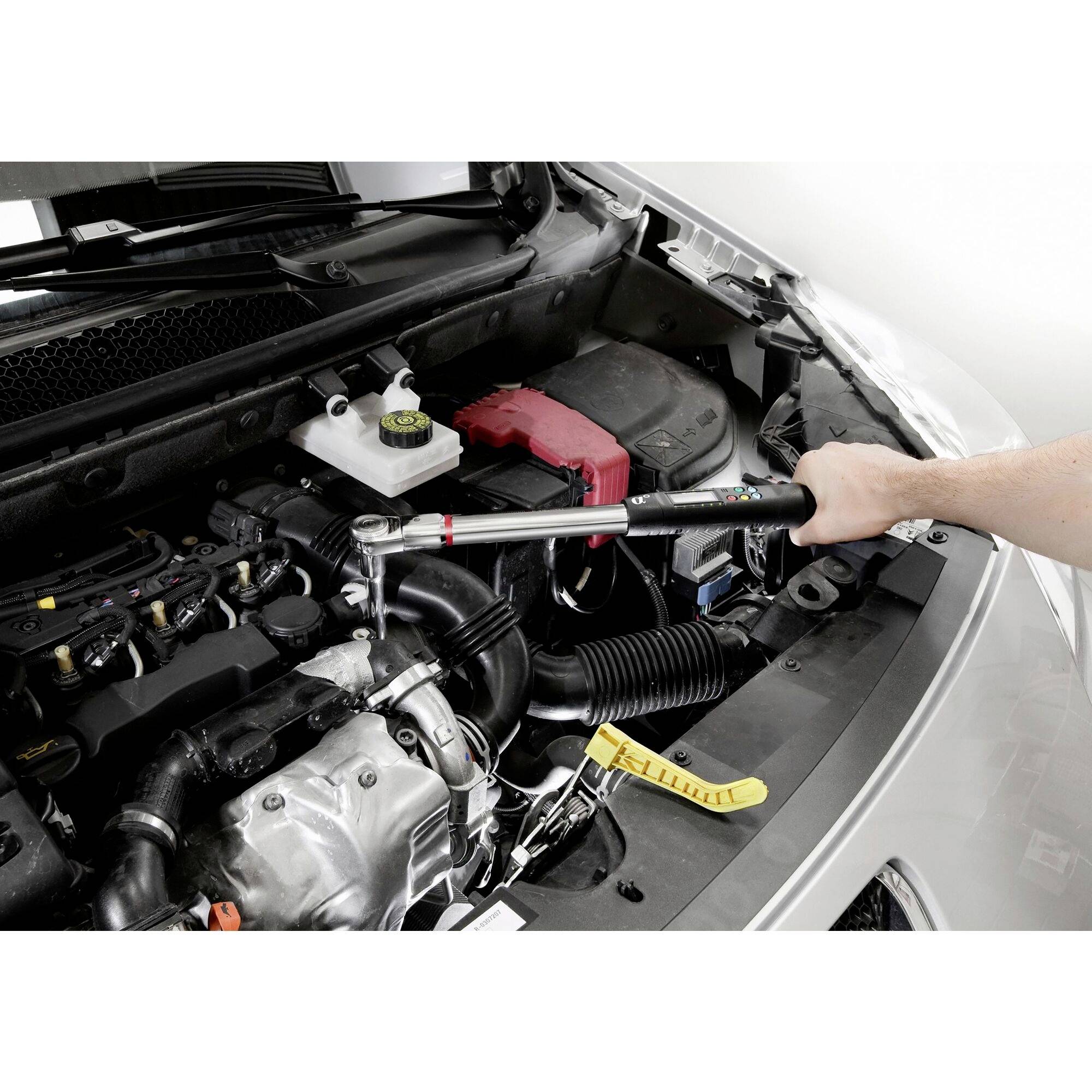 Une personne utilise une clé dynamométrique pour serrer une vis dans le compartiment moteur d'une voiture.