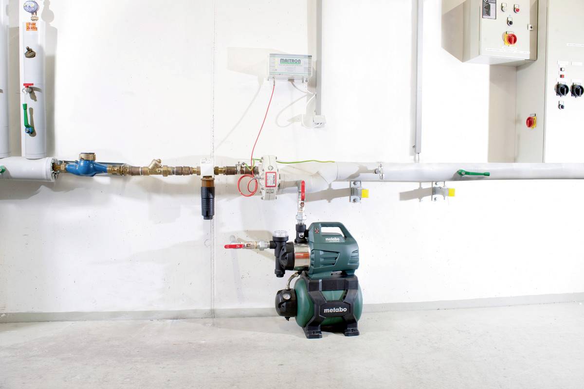 Une pompe à eau est raccordée à une conduite. En haut, des interrupteurs de commande et des appareils de mesure sont montés sur le mur.