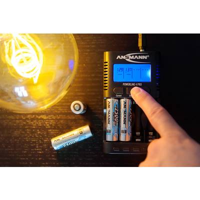 Une personne appuie sur une touche d'un chargeur de batterie à proximité de piles AA en cours de charge. Une ampoule est allumée en arrière-plan.