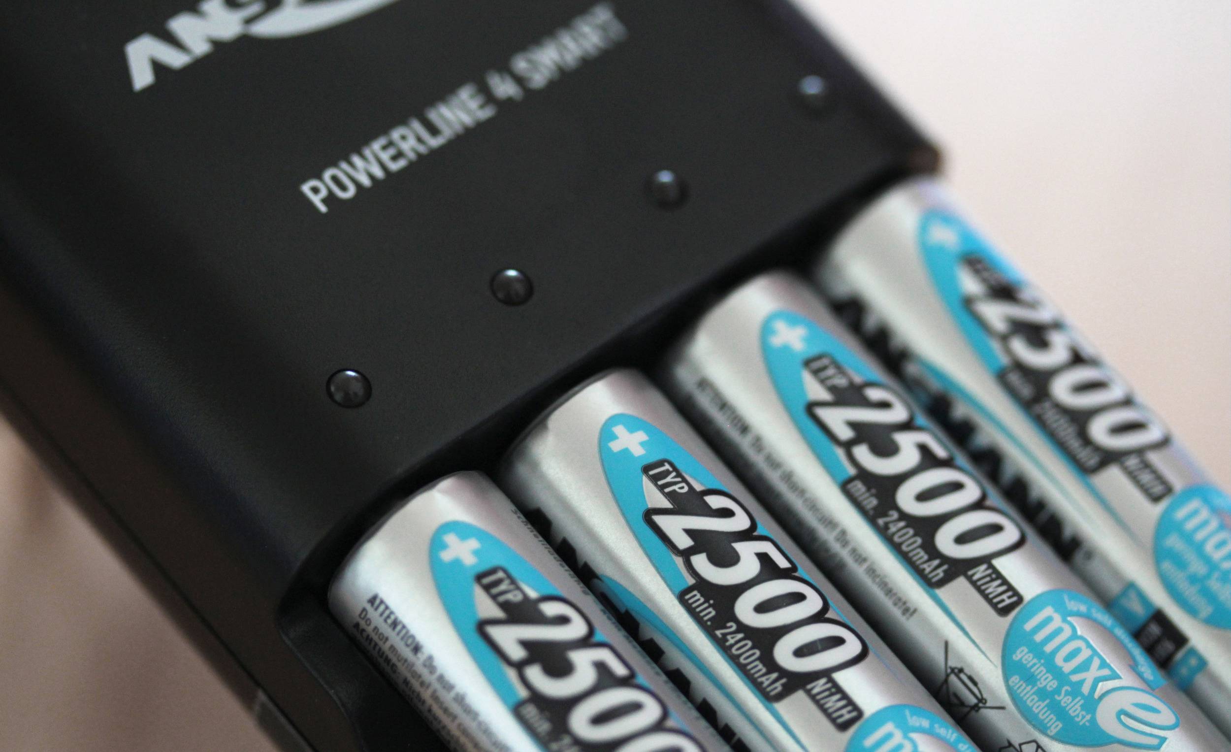 Un chargeur de batterie noir charge quatre piles AA argentées, chacune portant l'inscription « 2500 mAh ».