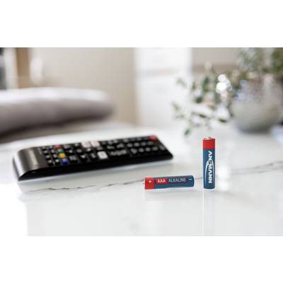 Une télécommande est posée sur une table, à côté de deux piles, l'une couchée ('AAA Alcaline') et l'autre debout.