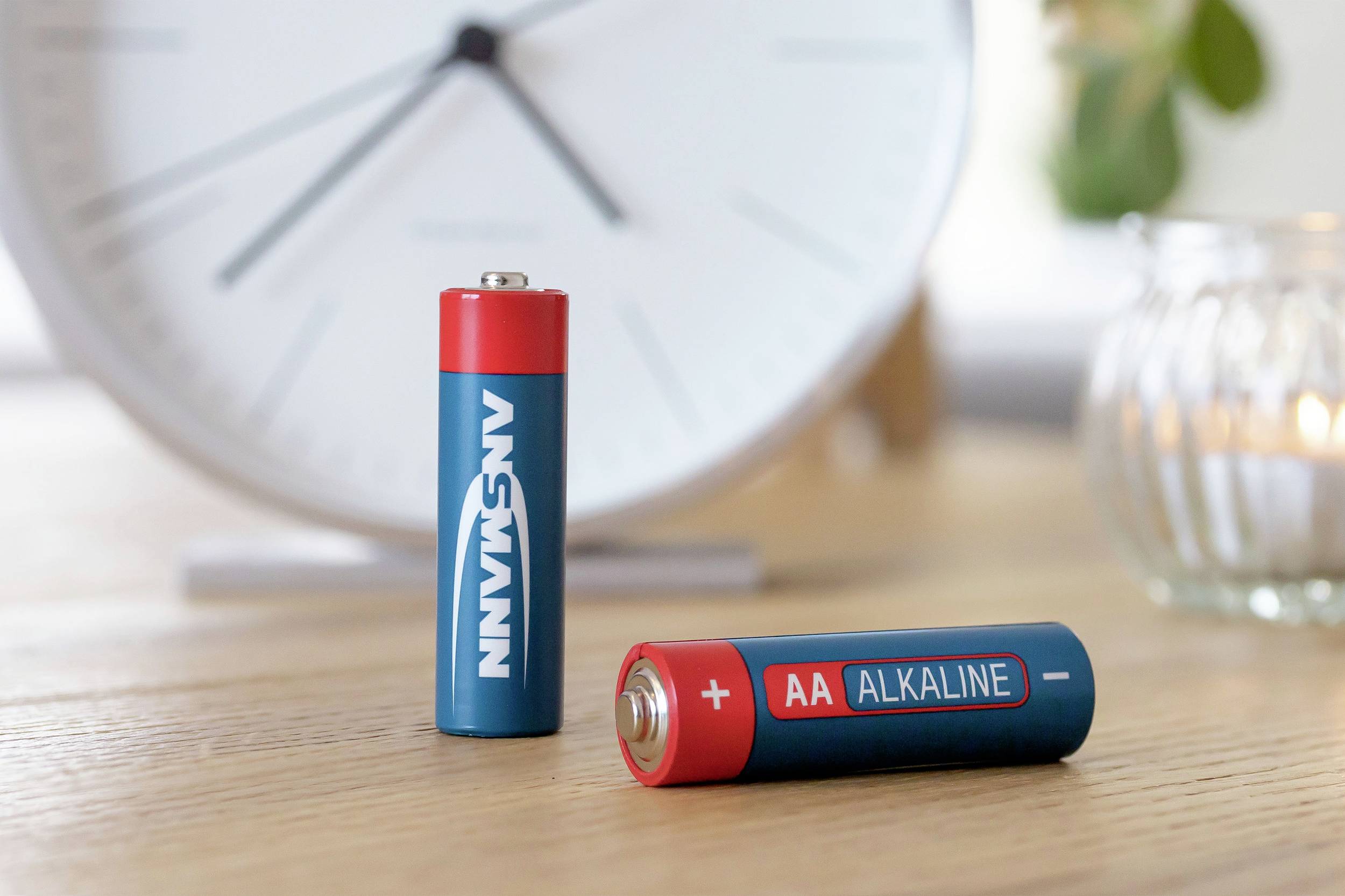 Deux piles AA, l'une debout, l'autre couchée, avec une horloge en arrière-plan.