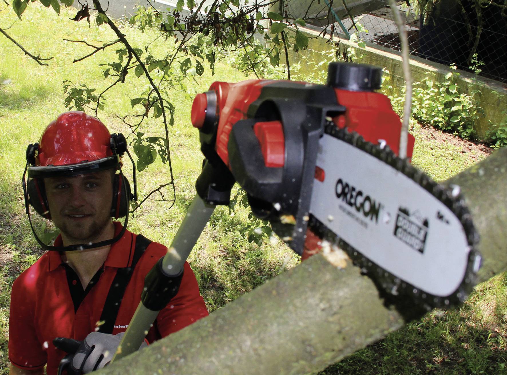 Une personne porte des vêtements de protection et utilise une tronçonneuse électrique à manche télescopique pour scier des branches d'un arbre.