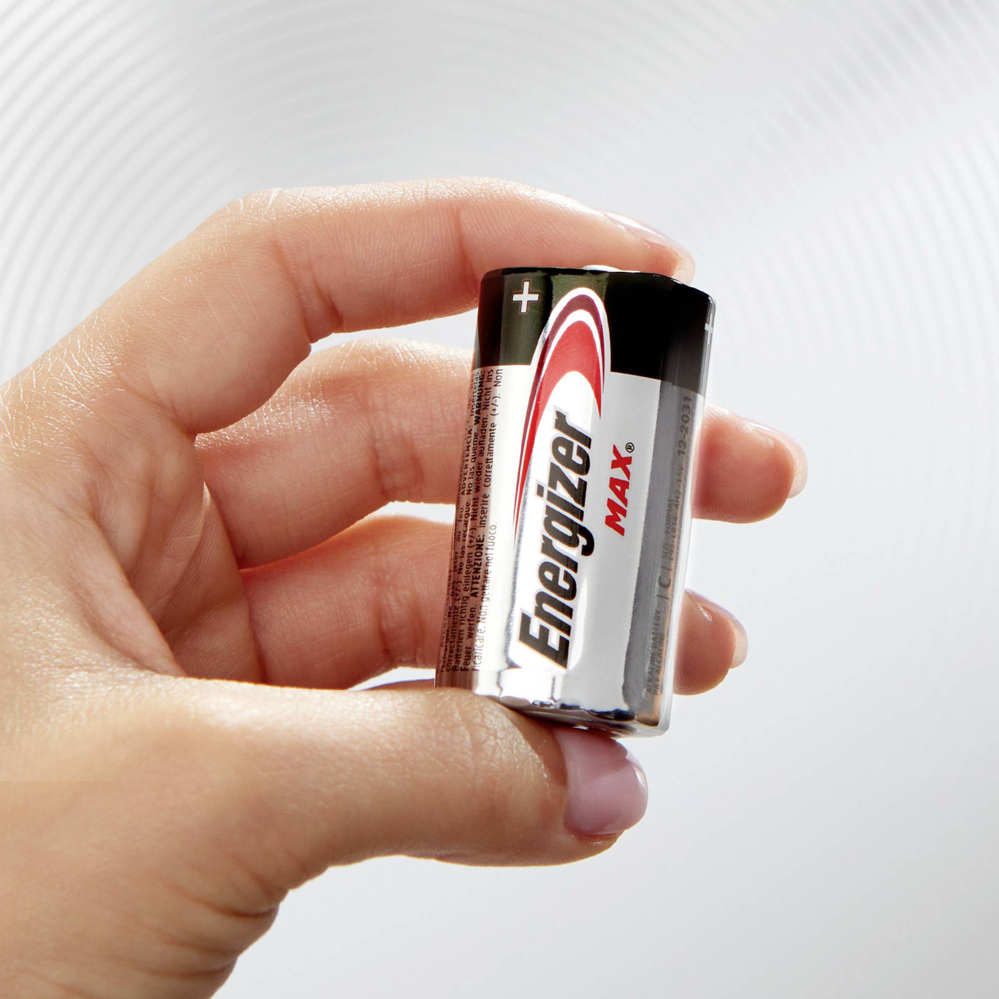 Une main tient une pile Energizer MAX, format C. Arrière-plan en motif concentrique blanc.