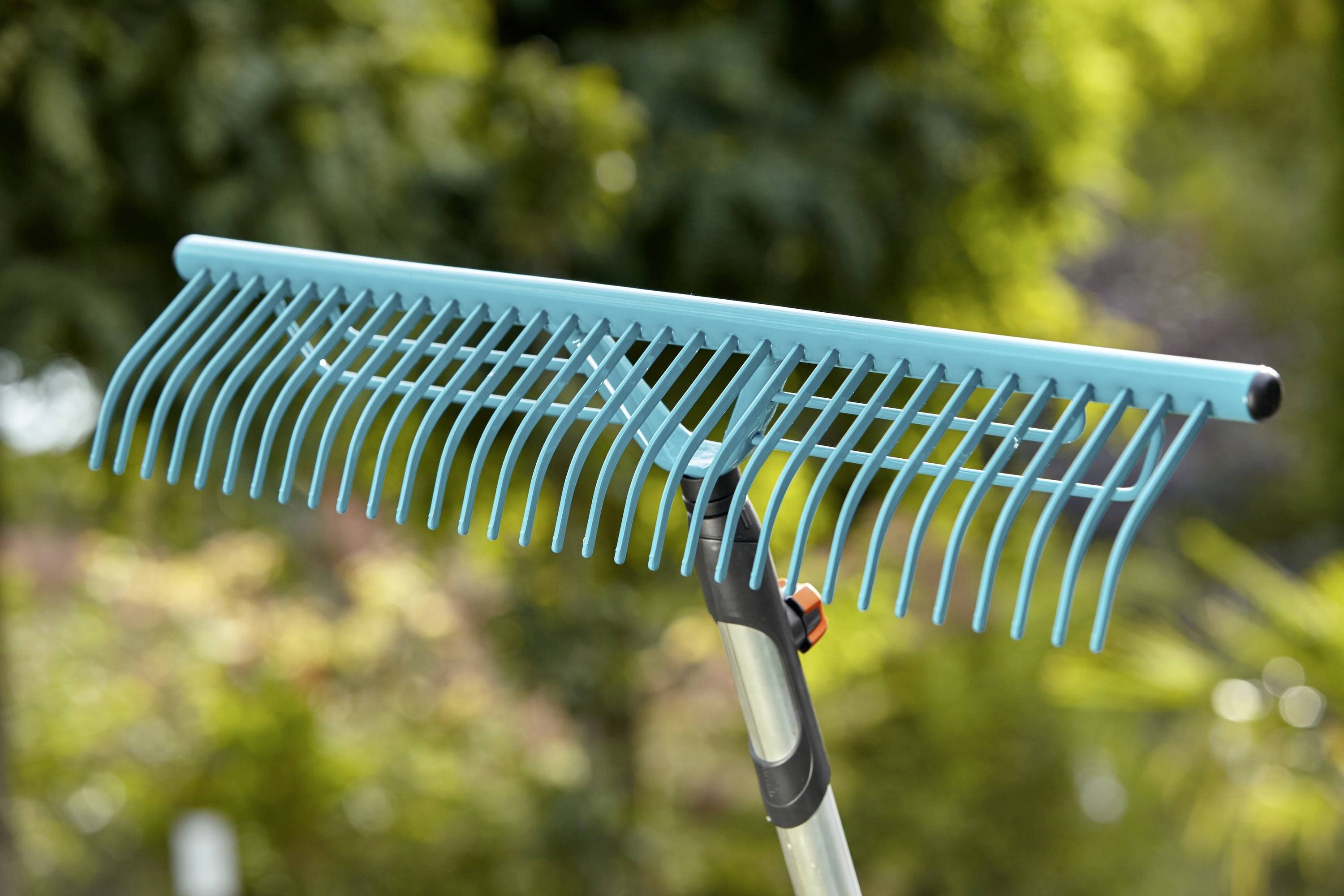 Un râteau bleu à feuilles devant un arrière-plan vert flou, prêt à ramasser des feuilles ou des déchets de jardin.
