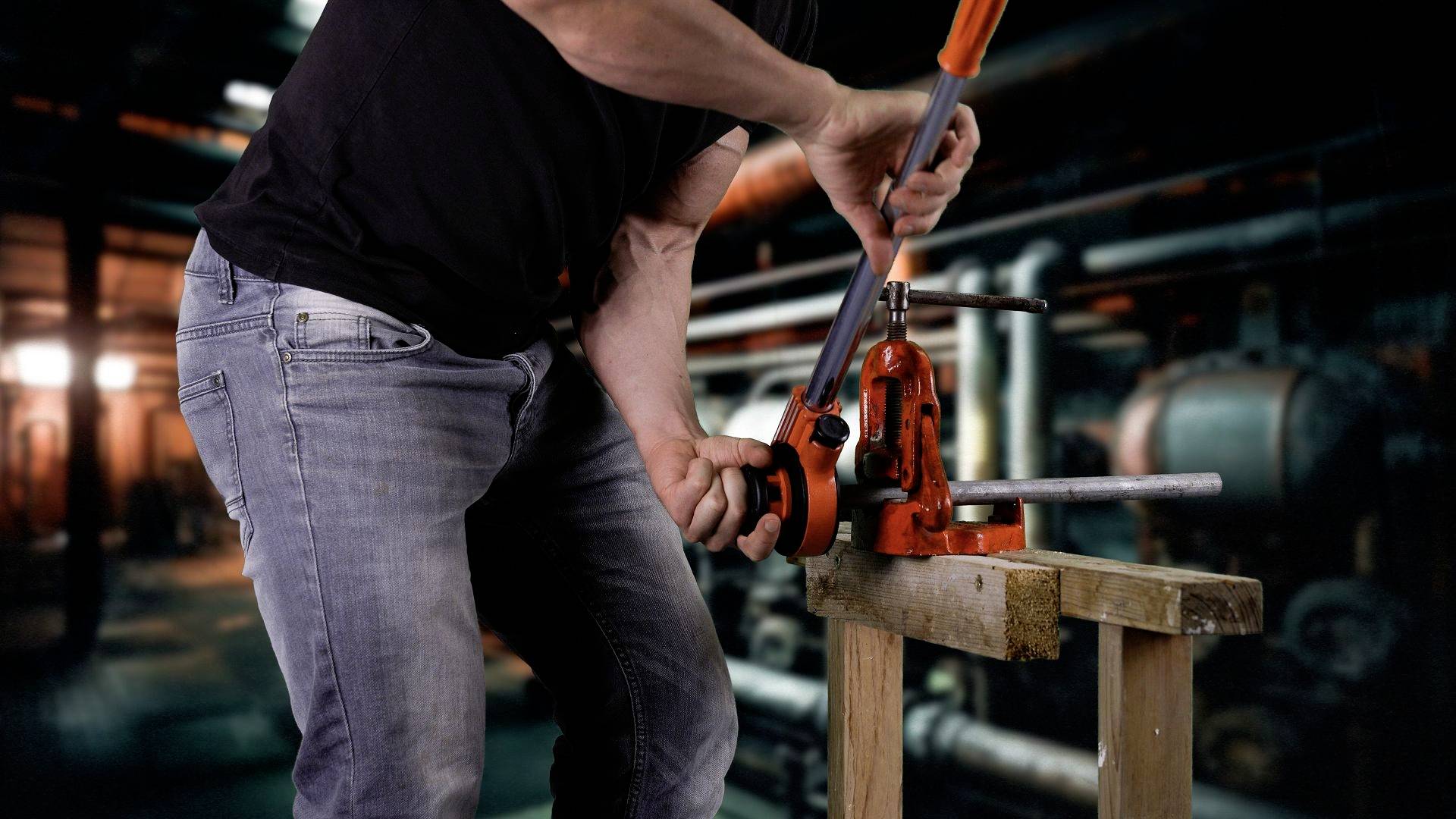 Une personne travaille dans un atelier et utilise une machine à couper les tuyaux. Des tuyaux et des machines sont visibles en arrière-plan.