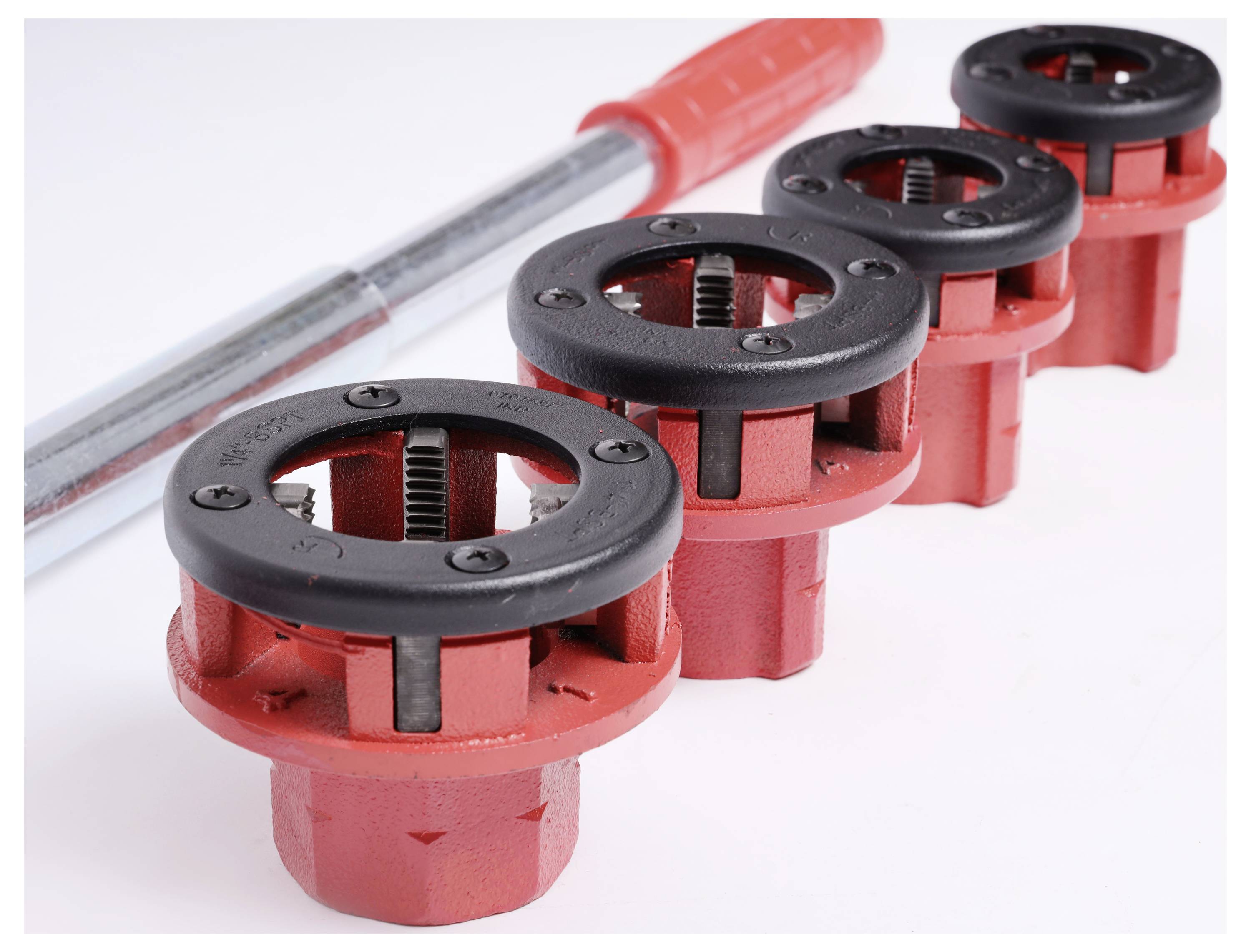 Quatre têtes de taraudage rouges et une longue poignée argentée sont posées sur une surface blanche.