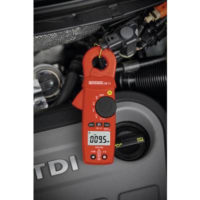 Un multimètre rouge affiche 009,5 mA et est fixé à un câble dans un espace de moteur. Des pièces de moteur sont visibles en arrière-plan.