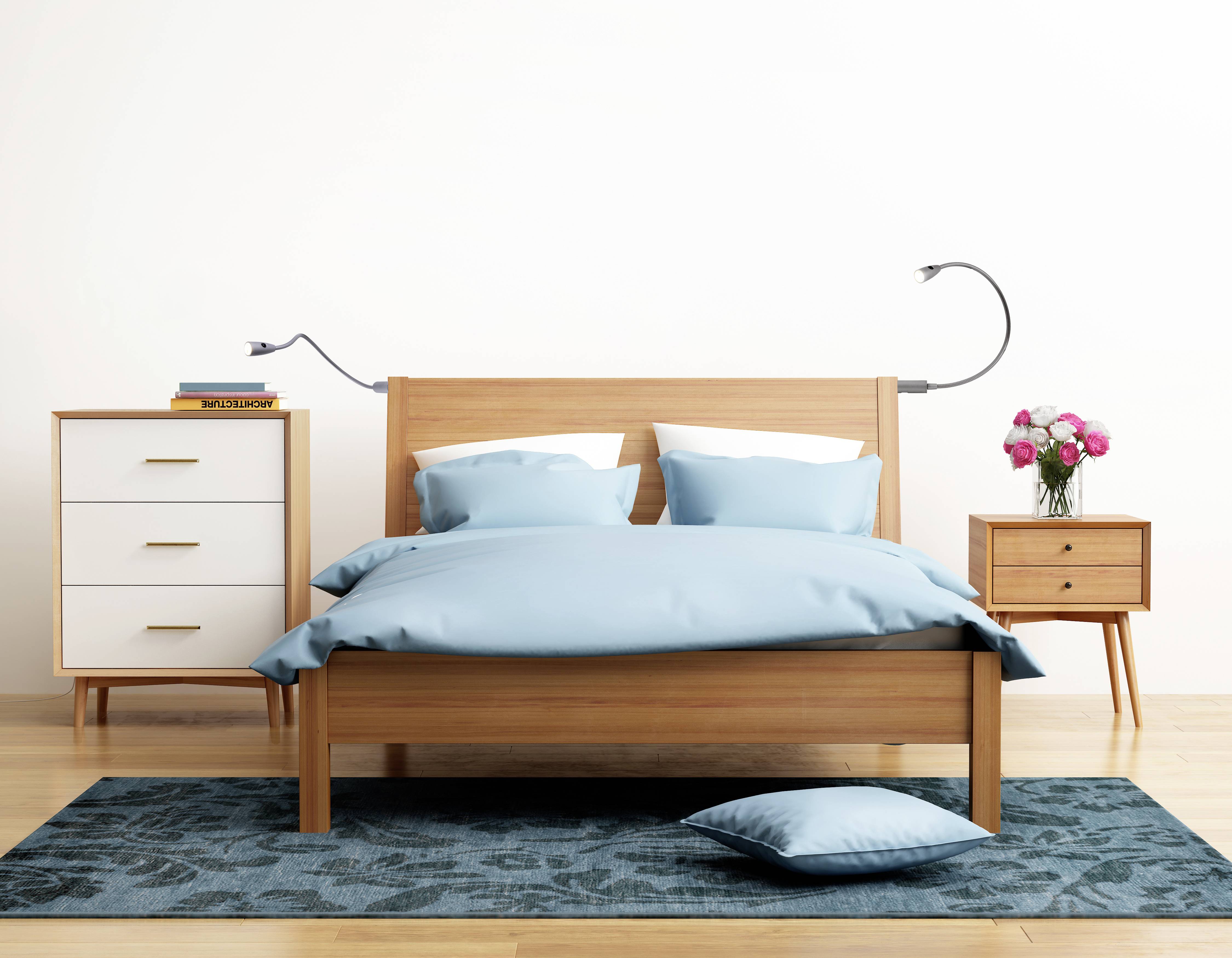 Une chambre à coucher avec un lit double en bois, des draps bleus, une table de chevet et une commode. Un vase avec des fleurs roses est posé sur la table de chevet.