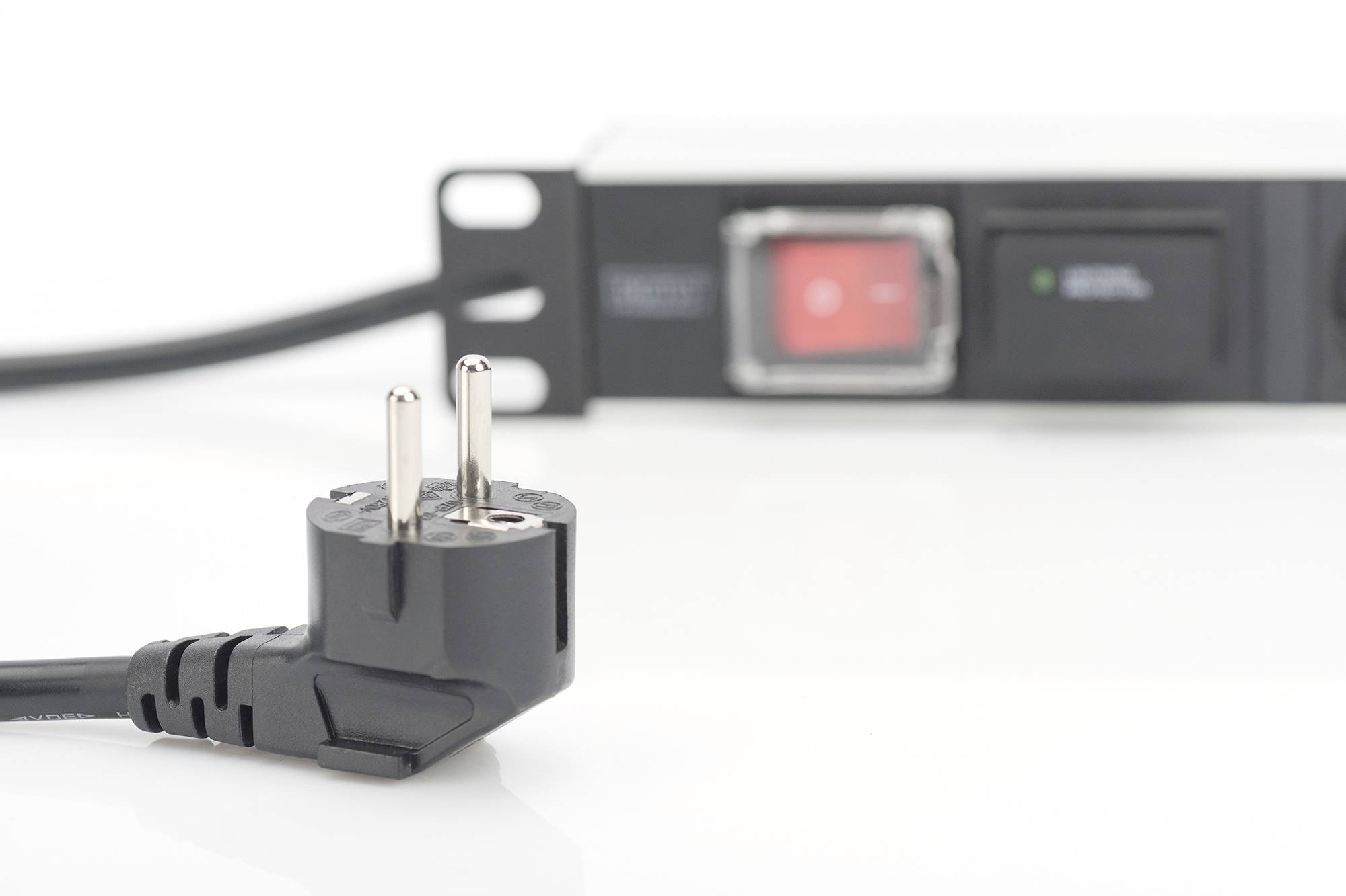 Un connecteur Schuko noir est au premier plan, avec un module de gestion de l'alimentation en rack, flou en arrière-plan, équipé d'un interrupteur.