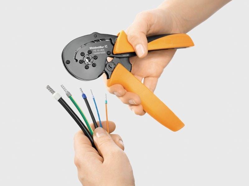 Deux mains manipulent une pince de câble orange. Une main maintient la pince, l'autre plusieurs torons de câbles isolés en dessous.