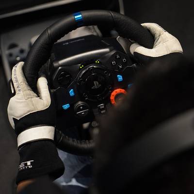 Une personne portant des gants tient un volant de jeu arborant le logo PlayStation, prêt pour une simulation de course.