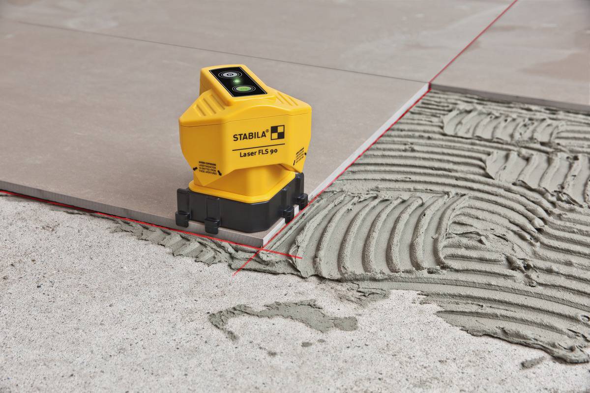 Laser à lignes croisées jaune de la marque STABILA projetant des lignes rouges sur des carrelages et du ciment afin de permettre un alignement précis.