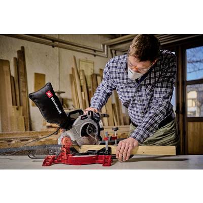 Un homme travaille en toute sécurité avec une scie circulaire, portant des lunettes de protection et un masque respiratoire. Des outils en bois sont visibles en arrière-plan.