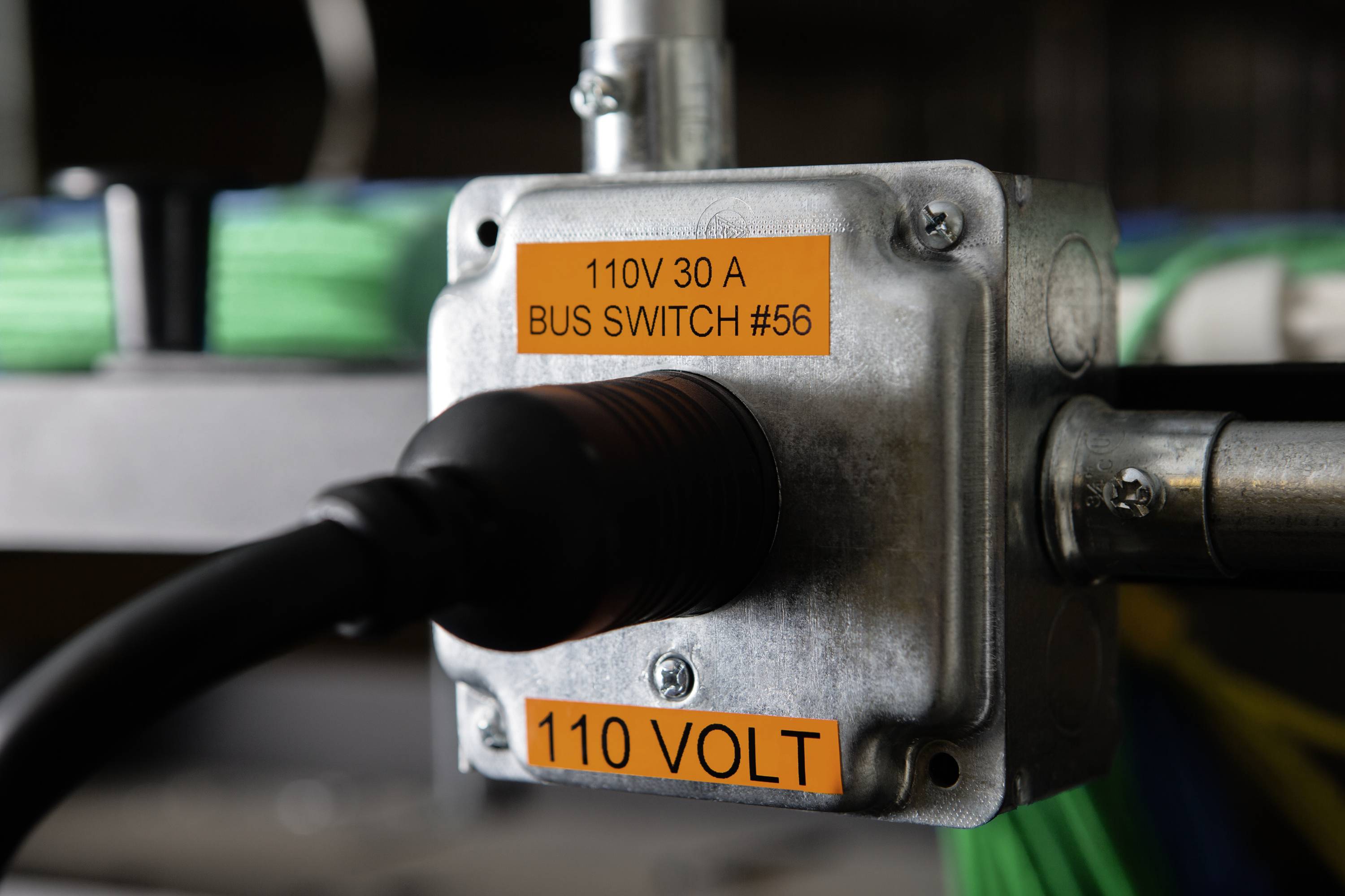 Boîte métallique avec câble noir ; autocollant orange : '110V 30 A BUS SWITCH #56' et '110 VOLT'.