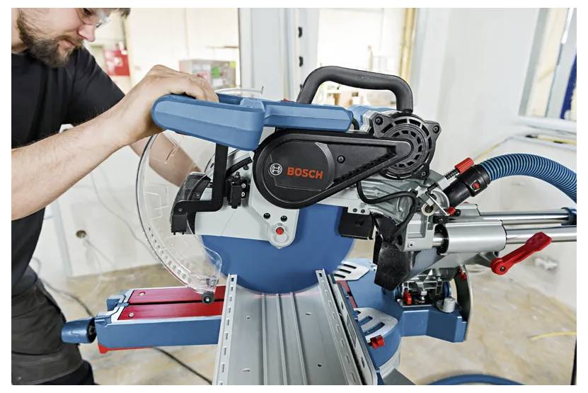 Un homme ajuste une scie à onglets Bosch sur un établi, se préparant à découper du matériau dans un atelier.