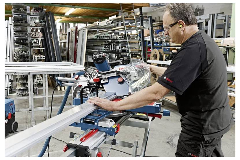 Des mains utilisant une défonceuse Bosch montée dans une table de défonceuse à plongeur pour le travail du bois sur un établi en bois.
