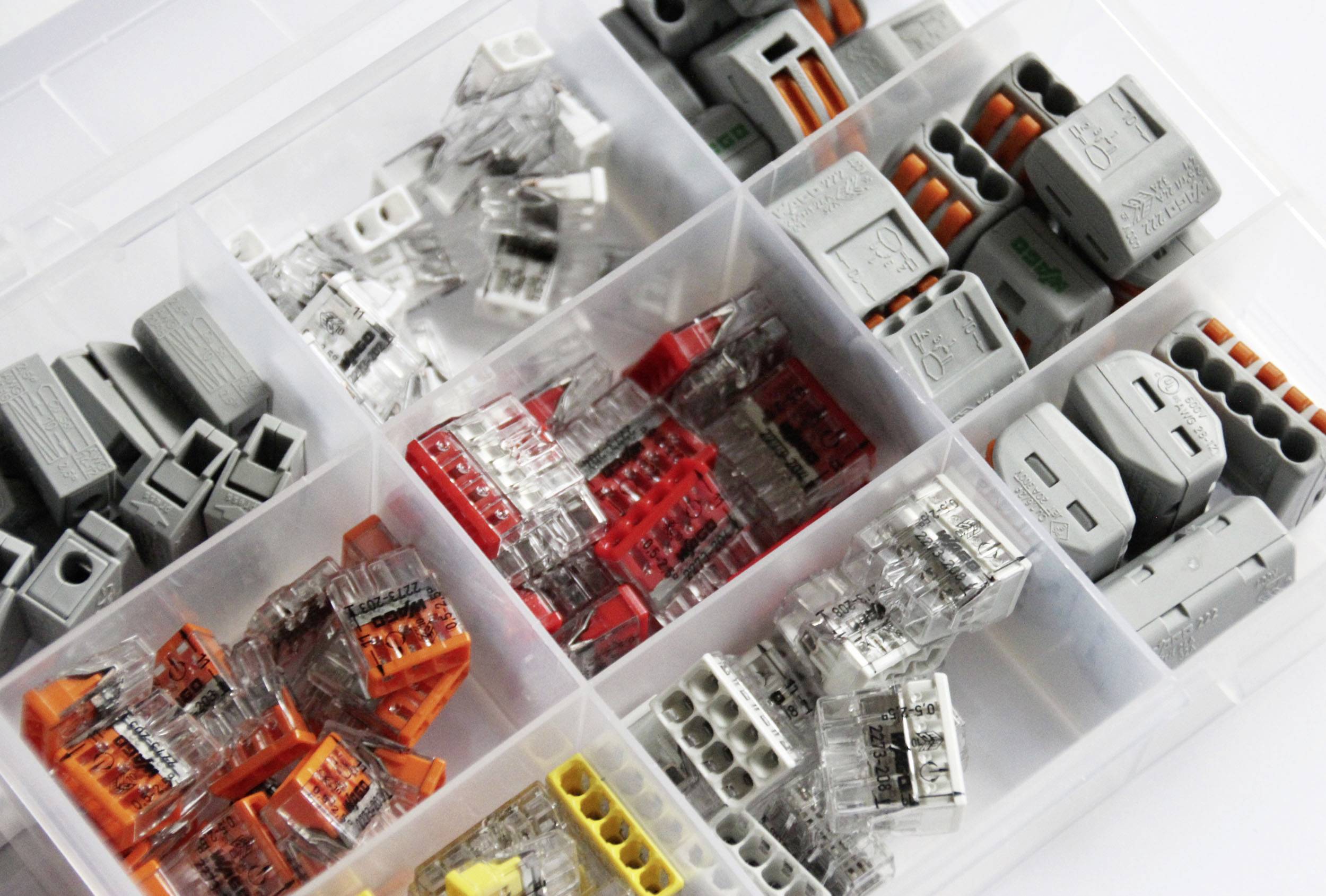 Une boîte d'assortiment contenant différents connecteurs de câbles répartis dans plusieurs compartiments. Comprend des connecteurs transparents, gris, rouges et jaunes.