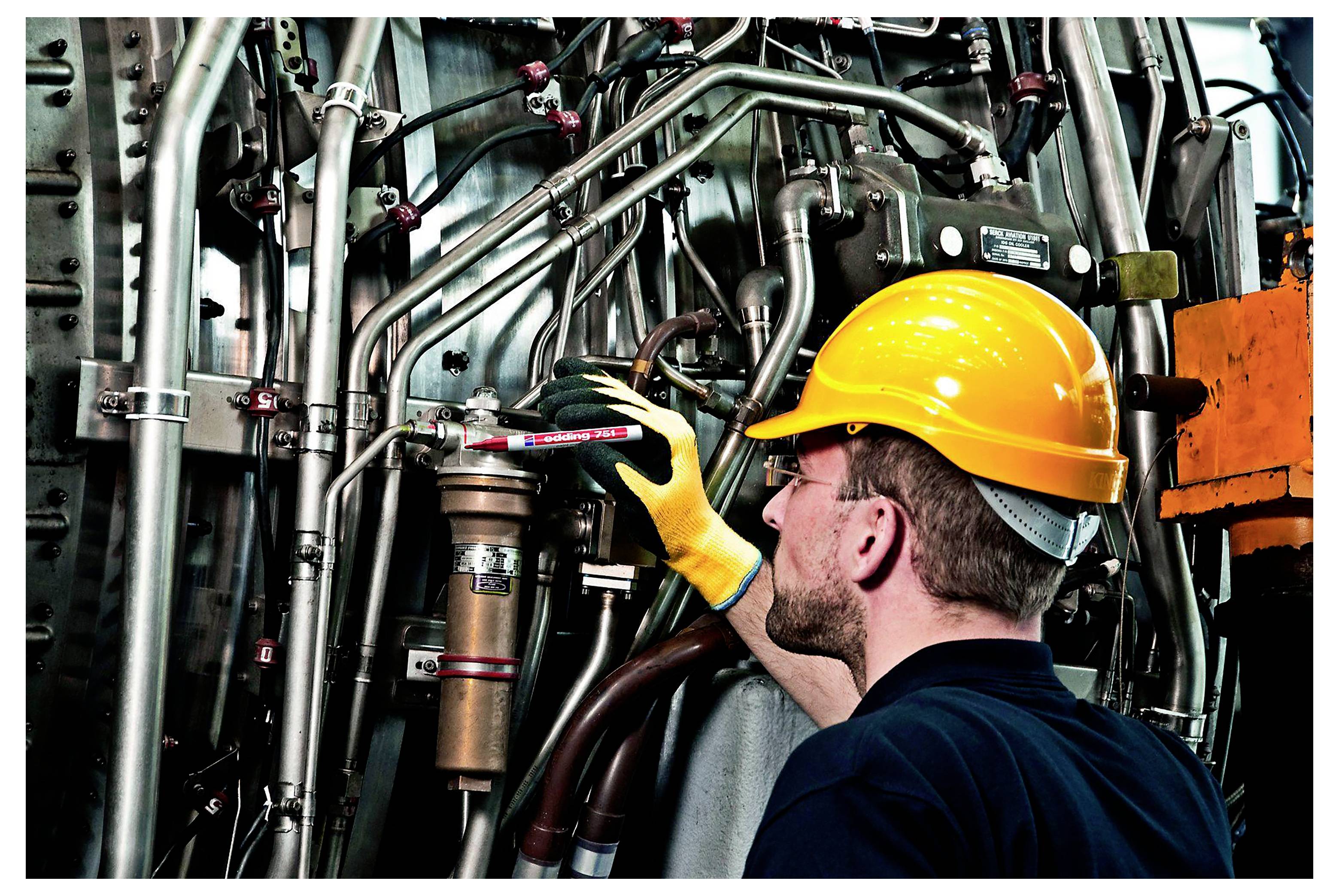 Un travailleur portant un casque de protection jaune et des gants inspecte les tuyauteries industrielles et les machines dans une usine ou une fabrique.