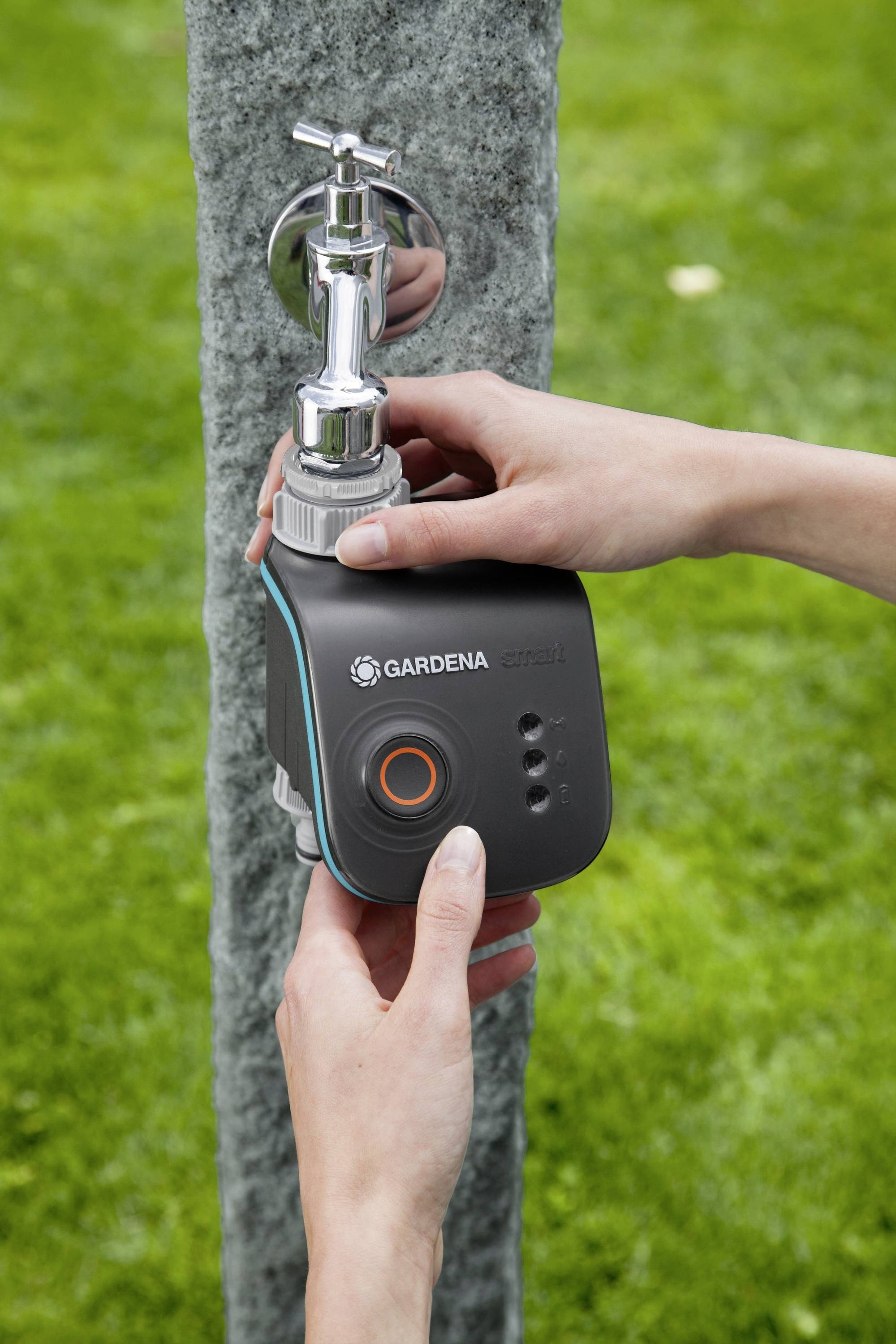 Deux mains installent un dispositif d'irrigation automatique sur un robinet de jardin.