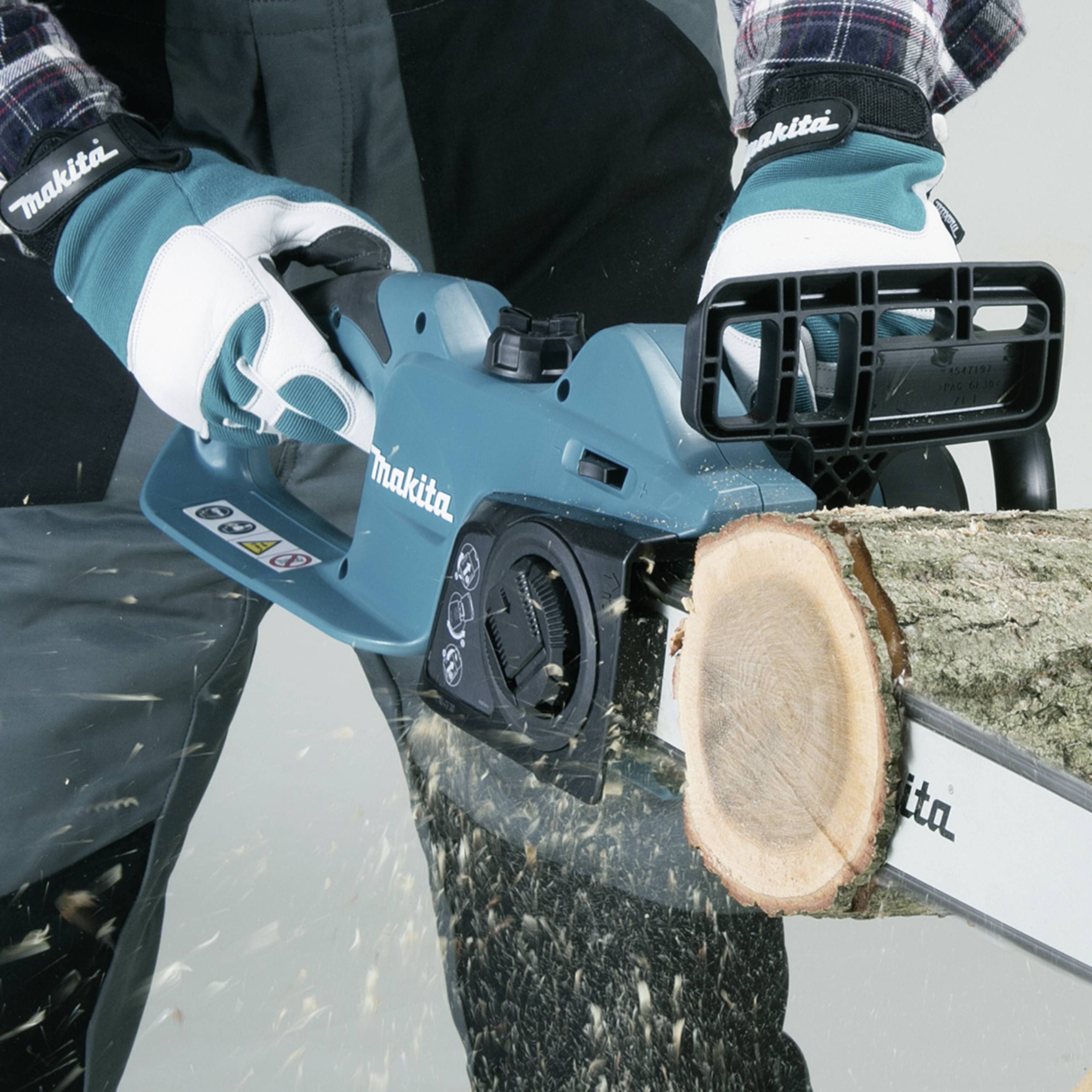 Une personne scie du bois avec une tronçonneuse bleue. La chaîne coupe à travers une branche. La personne porte des gants de travail.