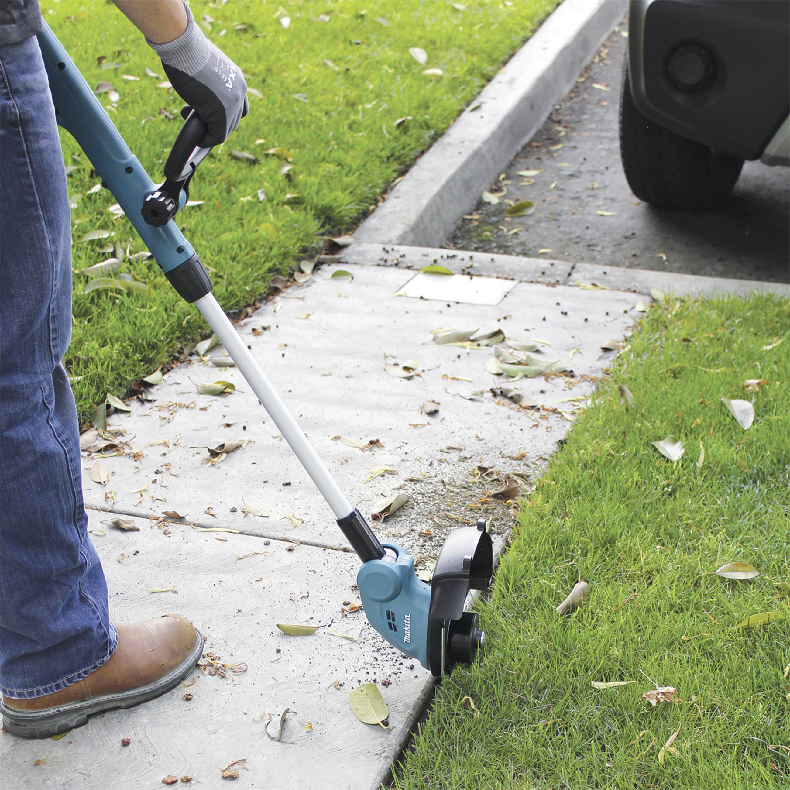 Une personne utilise un coupe-bordures électrique pour tailler les bords d'une pelouse le long d'un trottoir.