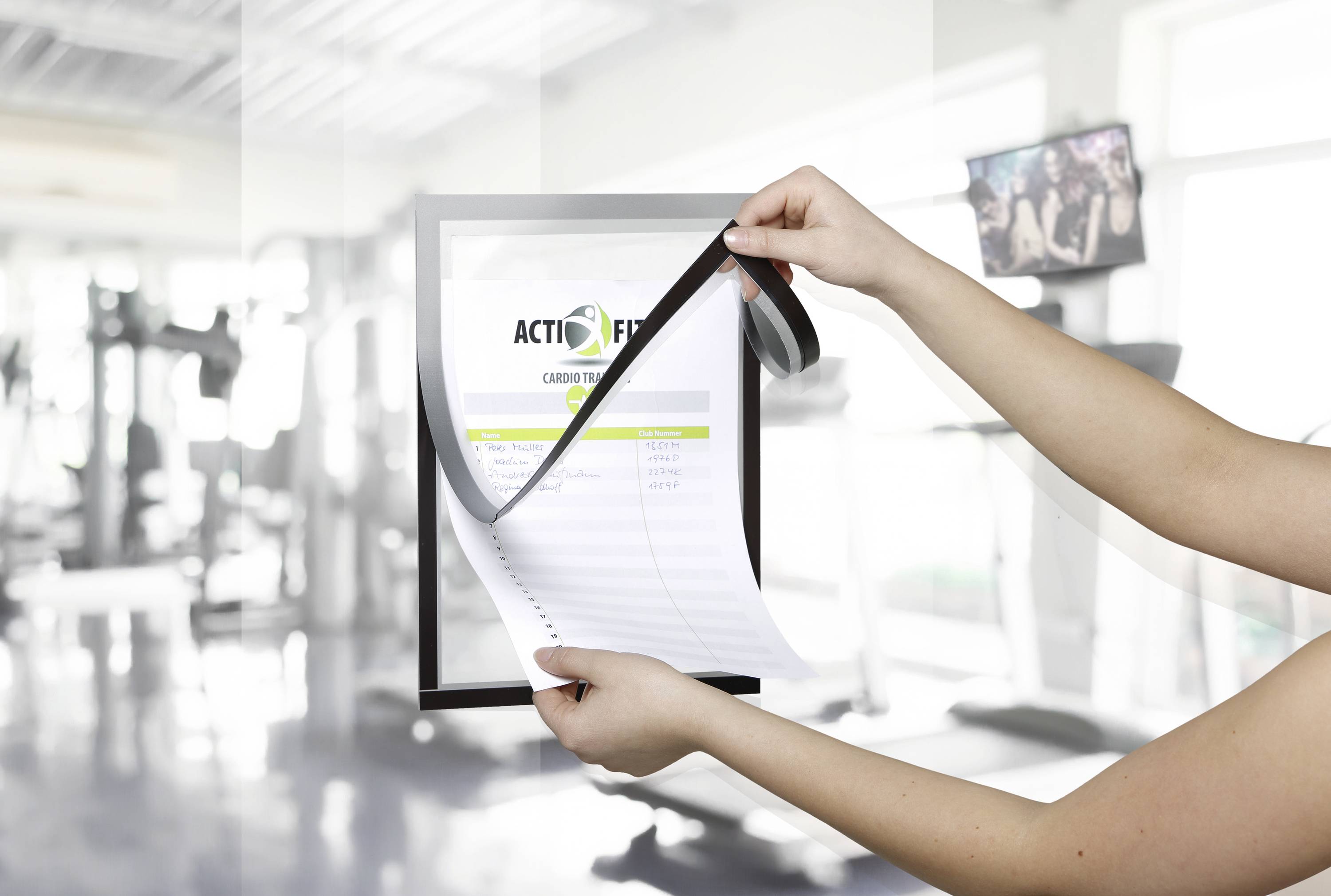 Une personne tient un cahier de plan de fitness dans une salle de sport, avec des équipements d'entraînement flous en arrière-plan.